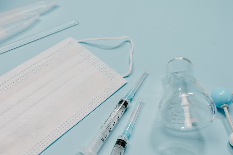 Close-up of surgical mask, syringes, and Erlenmeyer flask on a blue surface.